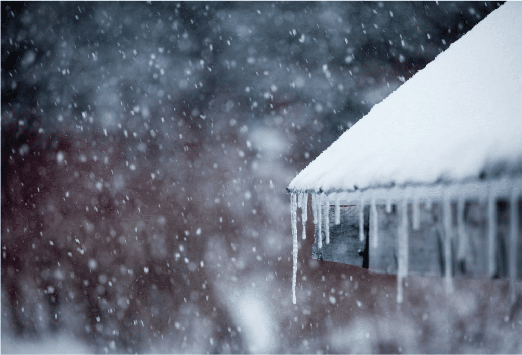 Snow-covered roof with long icicles forming along the edge during a winter snowfall.